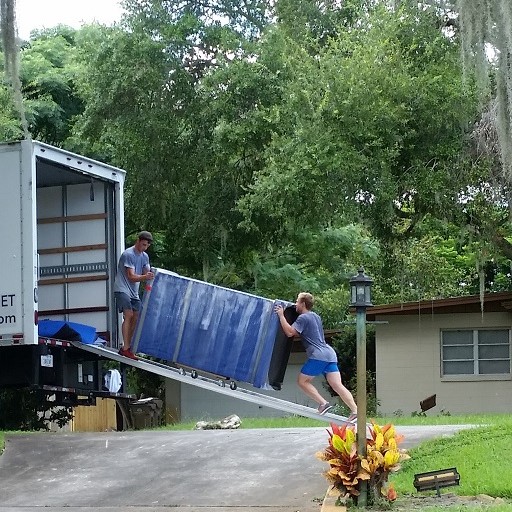 2 strong movers pushing a couch on a dolly thru truck ramp.