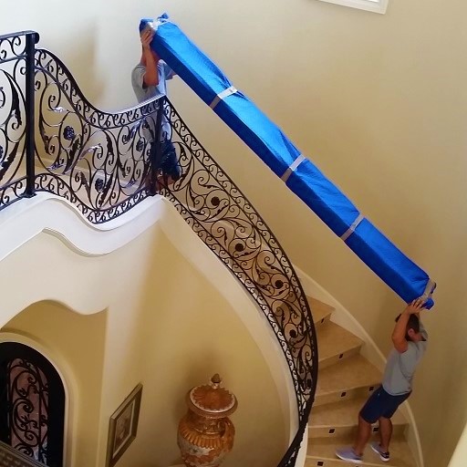 Round staircase of a house. 2 movers carefully moving a long piece of furniture.