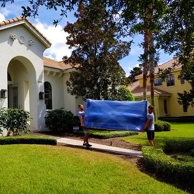 Movers in BALDWIN PARK- Big house. 2 movers moving a couch. couch is packed with moving blankets and wrapped with plastic. Location in Windermere FL