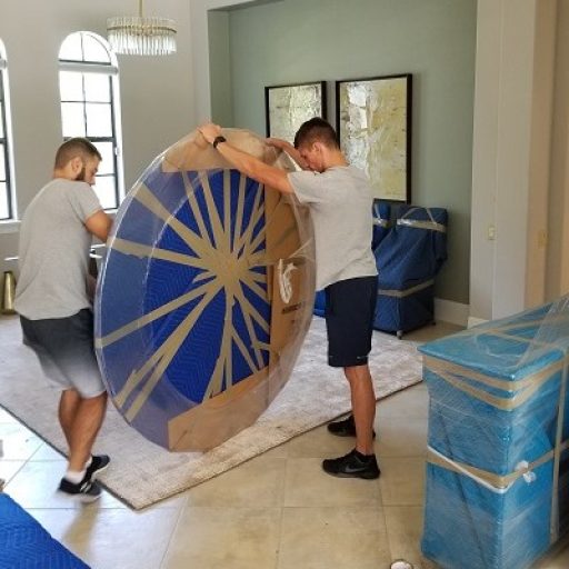 dinning area of a house. Movers packing a round table with plastic wrap, card board and tape.