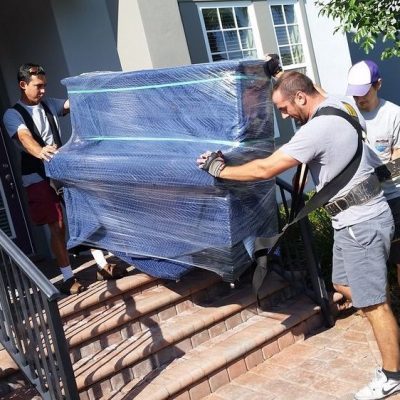 2 movers carring a piano with special shoulder straps out of HUNTERS CREEK HOUSE