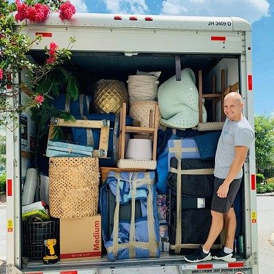 Back of the moving truck fully loaded. Smiling mover sitting stand up on the truck ramp.